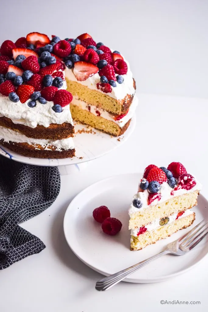 slice of cake on a white plate with fork beside cake stand with full cake and black kitchen towel
