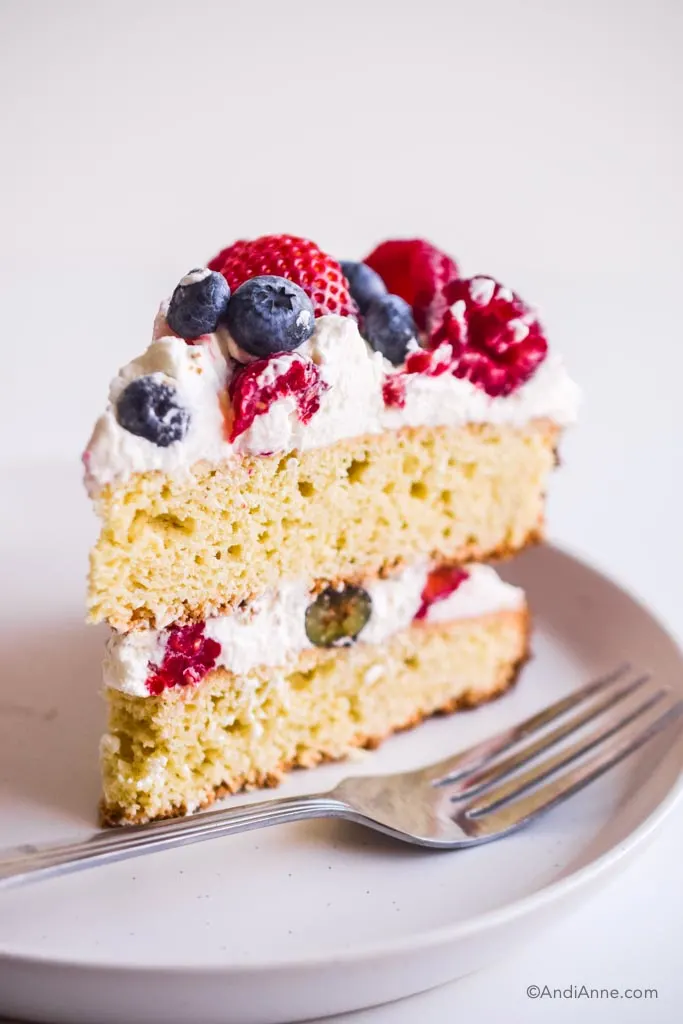 slice of gluten free white cake with whipped cream and berries in the center and on top
