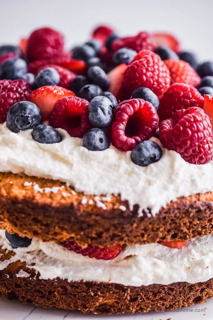 Close up detail of raspberries, blueberries, and strawberries on top of whipped cream and cake