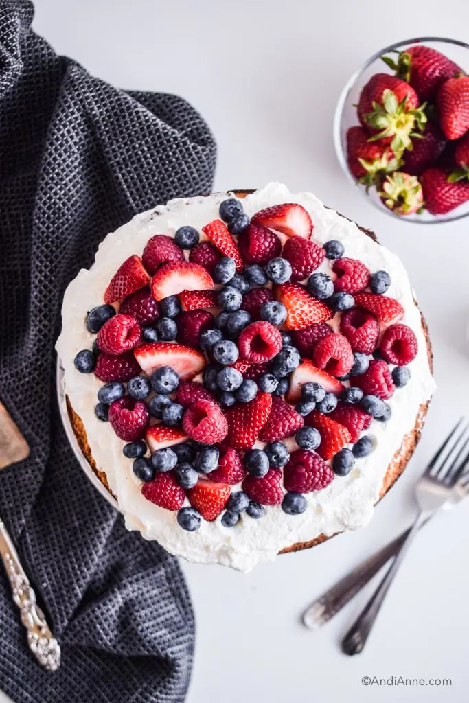 fresh berries on top of whipped cream with black kitchen towel, a glass bowl of strawberries and two forks