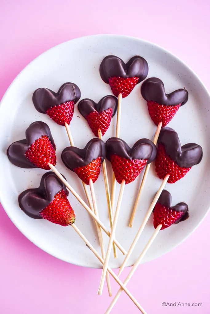 chocolate dipped heart strawberries on a white plate with a pink background