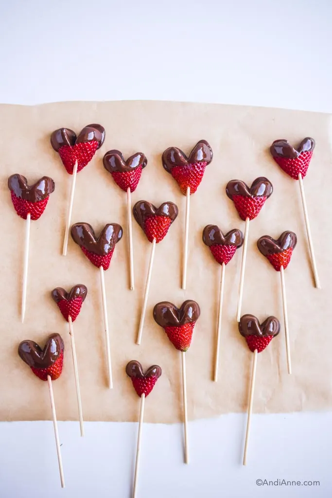 chocolate dipped heart strawberries poked with skewers and on brown parchment paper