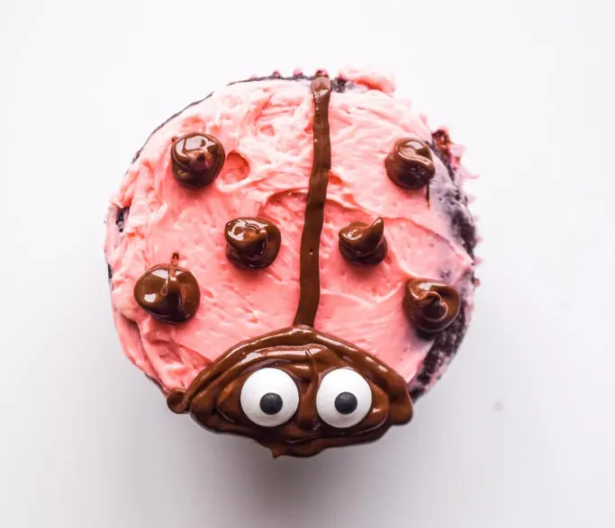 ladybug cupcake design with pink icing and chocolate and eyeball candies
