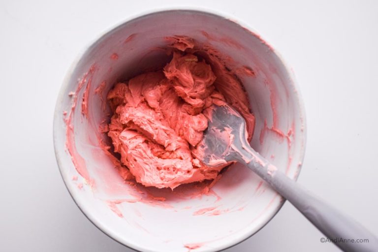 pink icing in a white bowl with spatula
