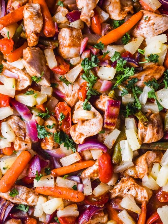 close up of everything inside the pineapple chicken sheet pan dinner including chopped chicken, carrots, parsley, onion, and tomatoes