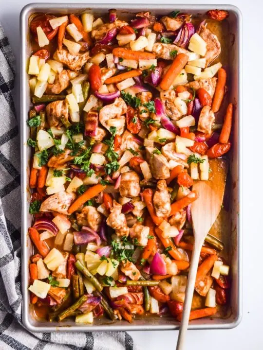 pineapple chicken sheet pan dinner with wood spatula and plaid checkered kitchen towel beside it