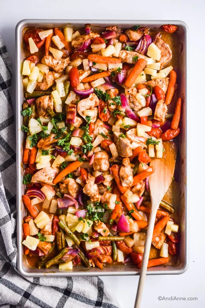 A sheet pan with vegetables and chicken and a wood spatula.