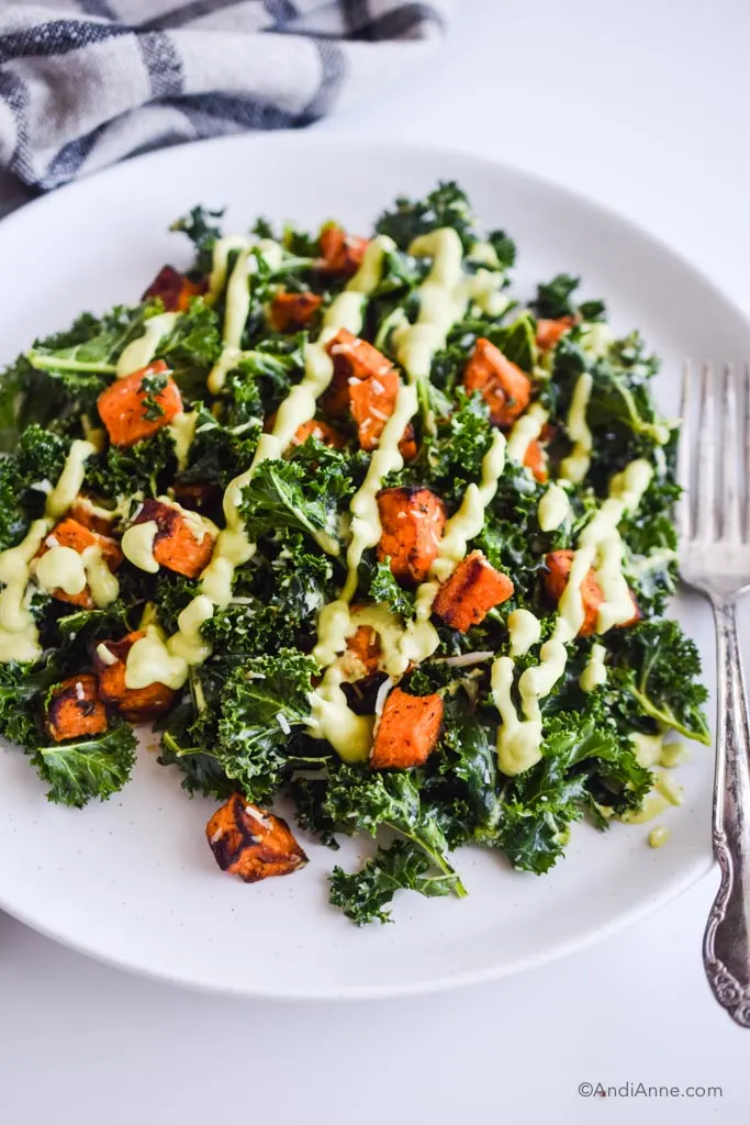 plate of sweet potato kale salad with a fork, drizzled with avocado dressing.