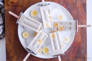 banana cream popsicles on white plate on wood cutting board