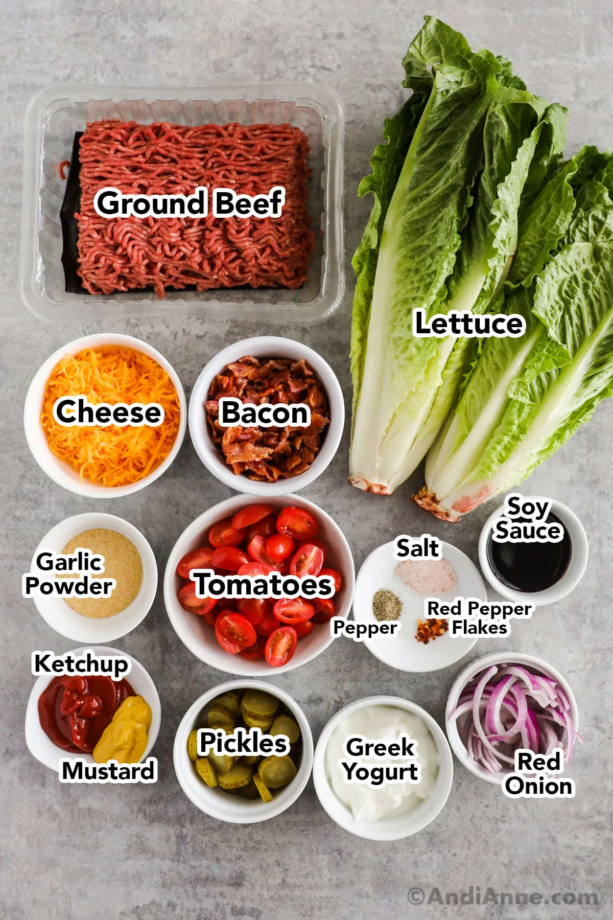 Recipe ingredients in bowls including cheese, bacon, tomatoes, greek yogurt, onions, pickles, spices, ground beef, romaine lettuce.
