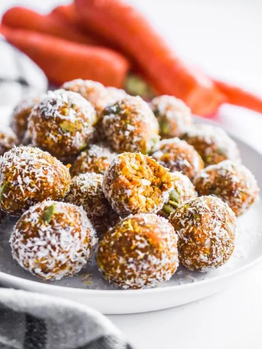 carrot cake bites on a white plate with carrots in the background