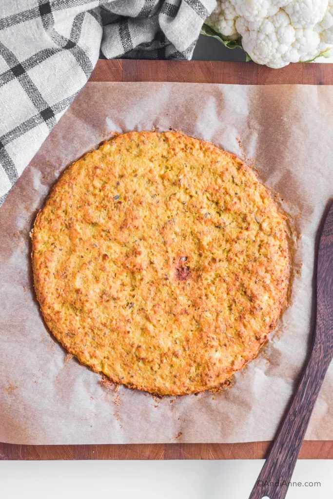 cauliflower pizza crust on a parchment paper with wooden spoon beside it