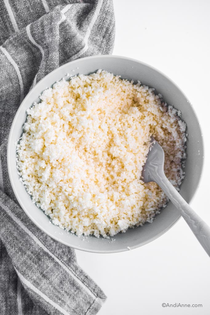 how to make riced cauliflower in a blue bowl with spatula and kitchen towel beside it