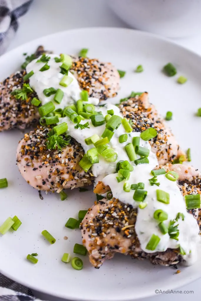 everything bagel chicken breasts on a white plate with greek yogurt dressing and sliced green onions sprinkled on top