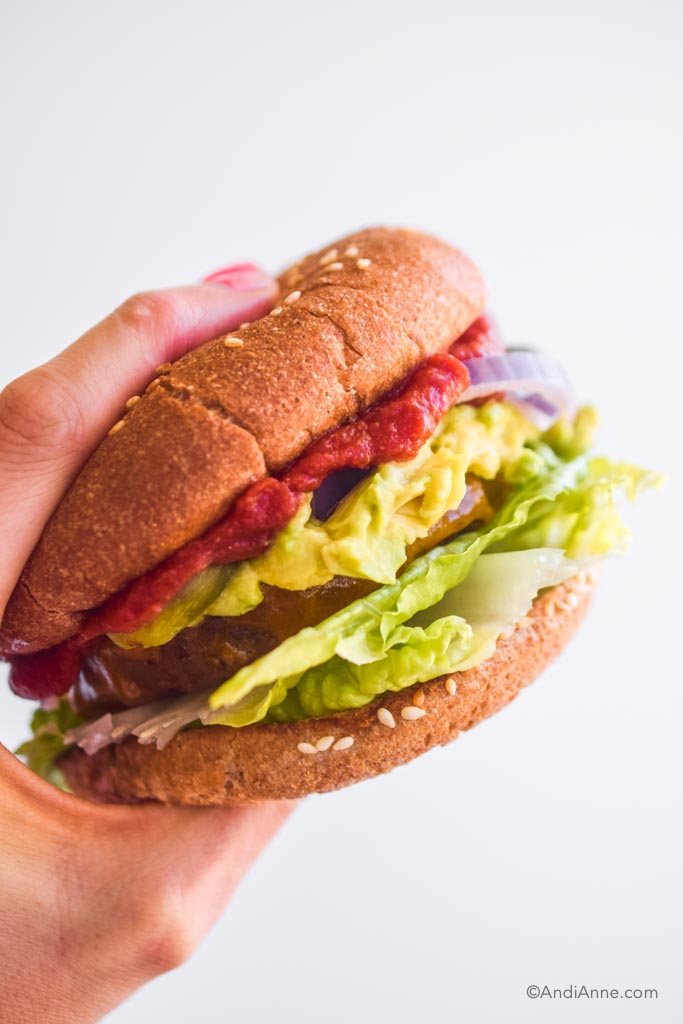 hand holding hamburger bun with lettuce avocado and ketchup