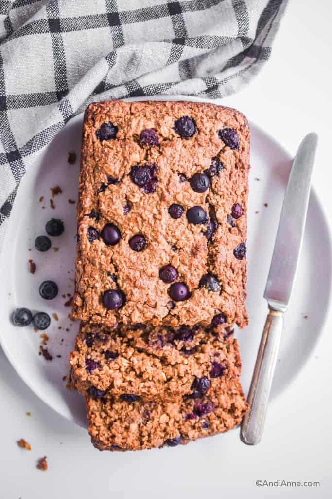 oatmeal blueberry breakfast loaf on white plate with a knife. Kitchen towel on the side of plate.