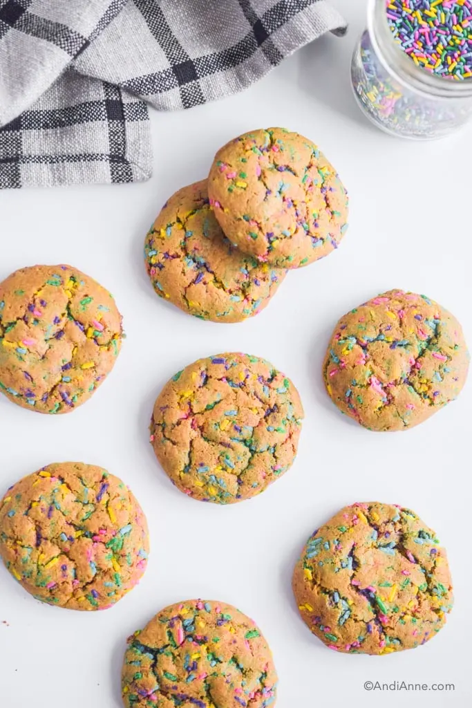 chickpea flour sprinkle cookies on a white counter with kitchen towel in and jar of sprinkles in top of photo