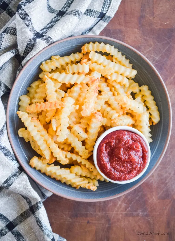 bowl of fries with ketchup in a dish on a cutting board.
