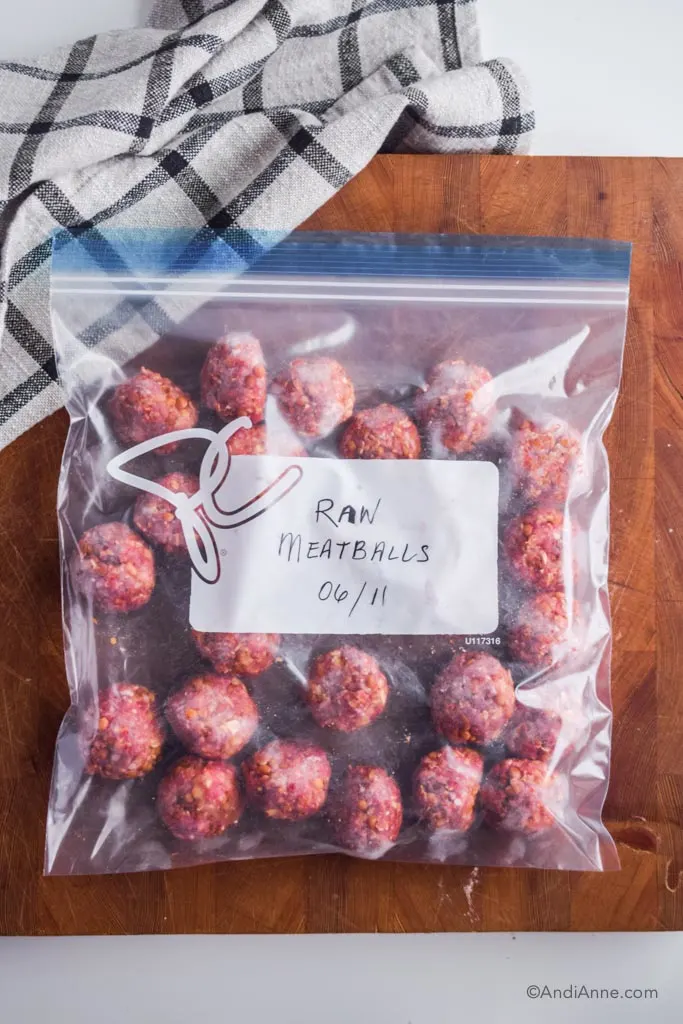 raw meatballs in a ziploc freezer bag on wood cutting board with kitchen towel beside it