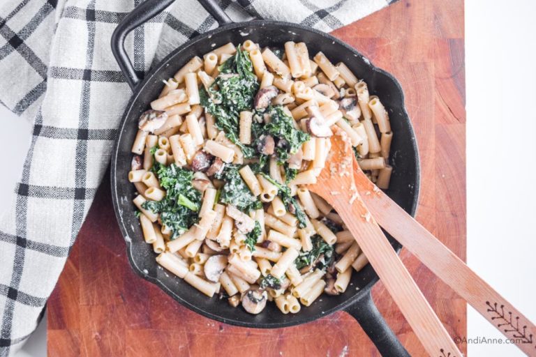 cooked pasta, kale and mushrooms with parmesan cheese in a frying pan. Two wooden spoons on the side.