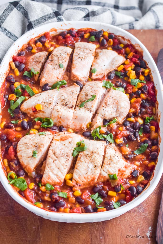 baked chicken breasts with black bean corn salsa in a white baking dish on wood cutting board