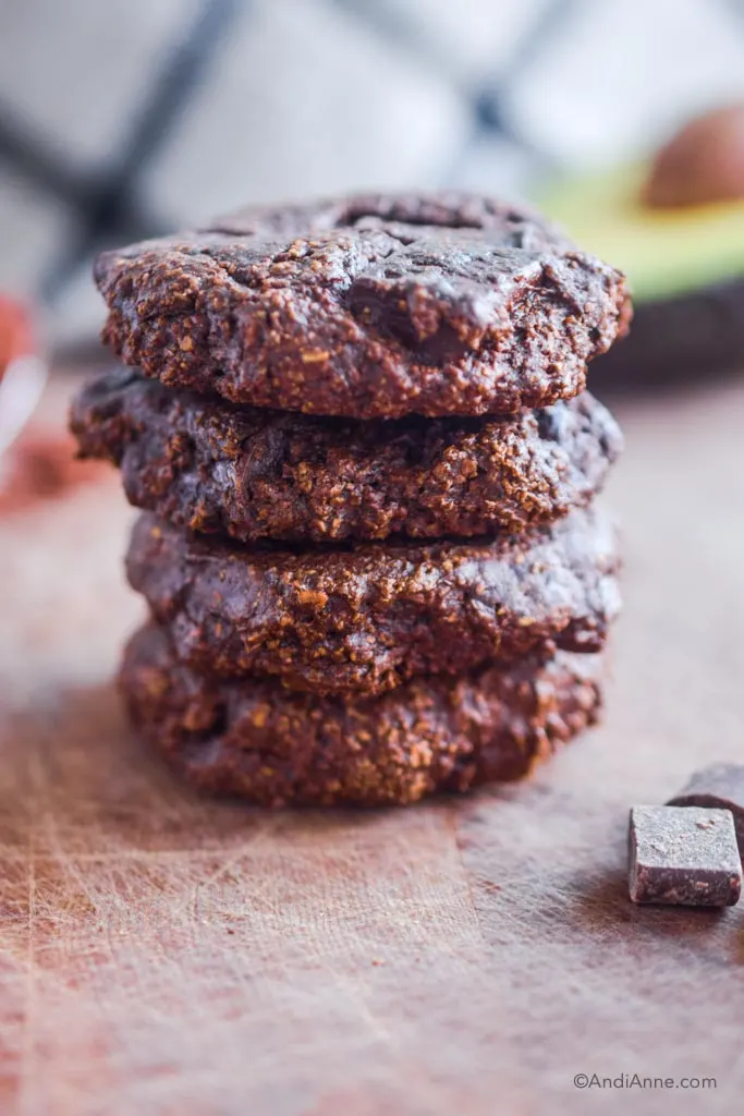 stacked chocolate avocado cookies on a cutting board with chocolate chunks beside it