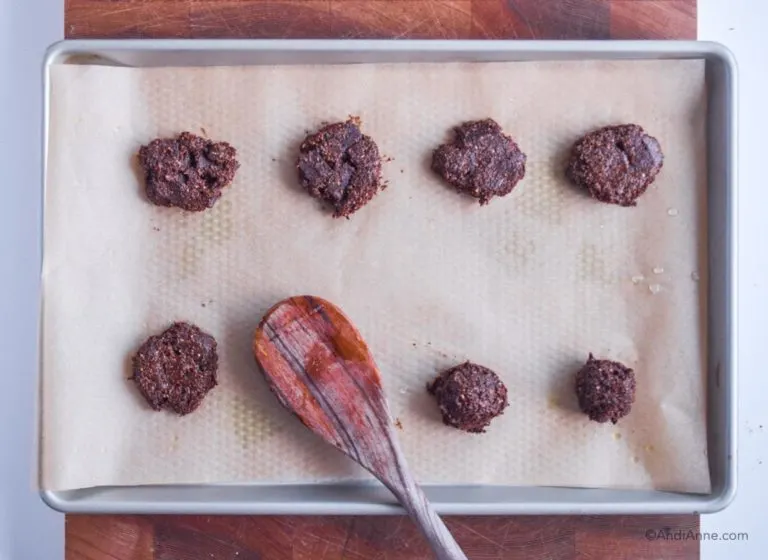 raw cookies on a baking sheet being flattened with back of a wooden spoon