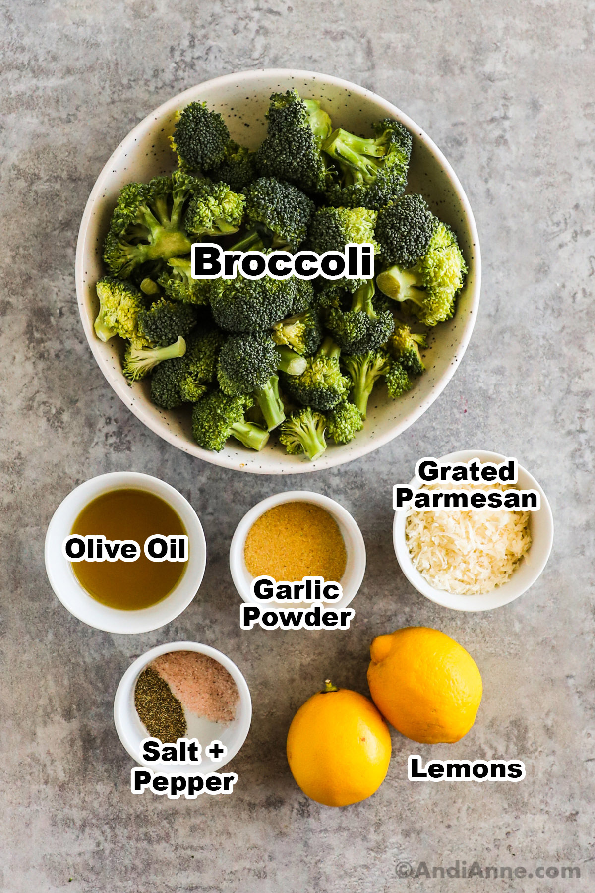 Recipe ingredients including bowls of broccoli florets, olive oil, garlic powder, grated parmesan cheese, salt and pepper and two lemons.