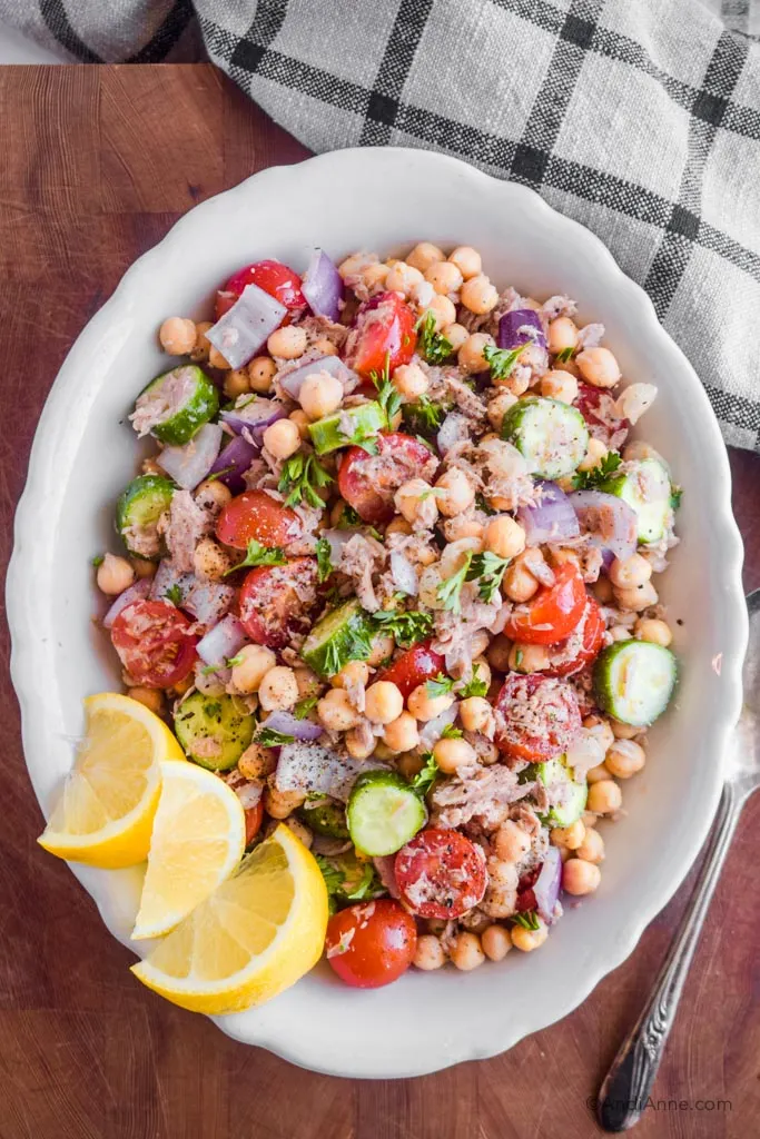chickpea lemon tuna salad in a white serving bowl with lemon wedges on the side.