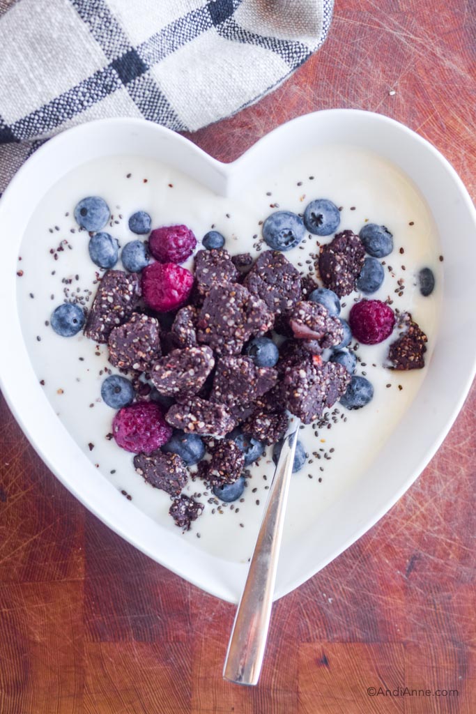 chocolate protein chia bites in a white heart-shaped bowl of yogurt with fresh berries.