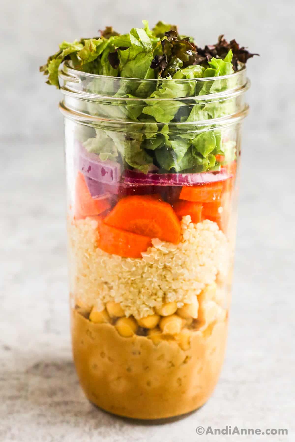 A nourish mason jar salad with chickpeas, quinoa, carrots, red onion and mixed greens.