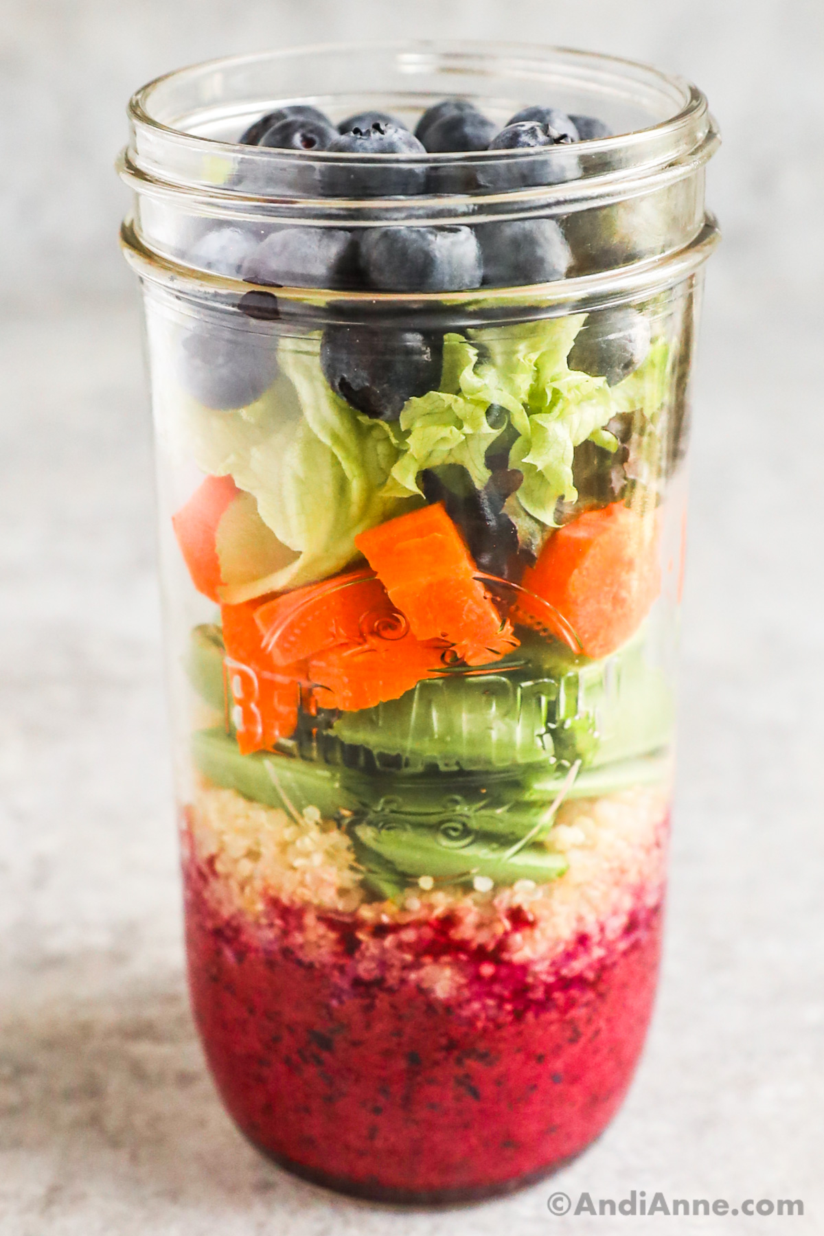 A mason jar salad with layers of blueberry dressing, quinoa, snap peas, carrots, mixed greens and blueberries.