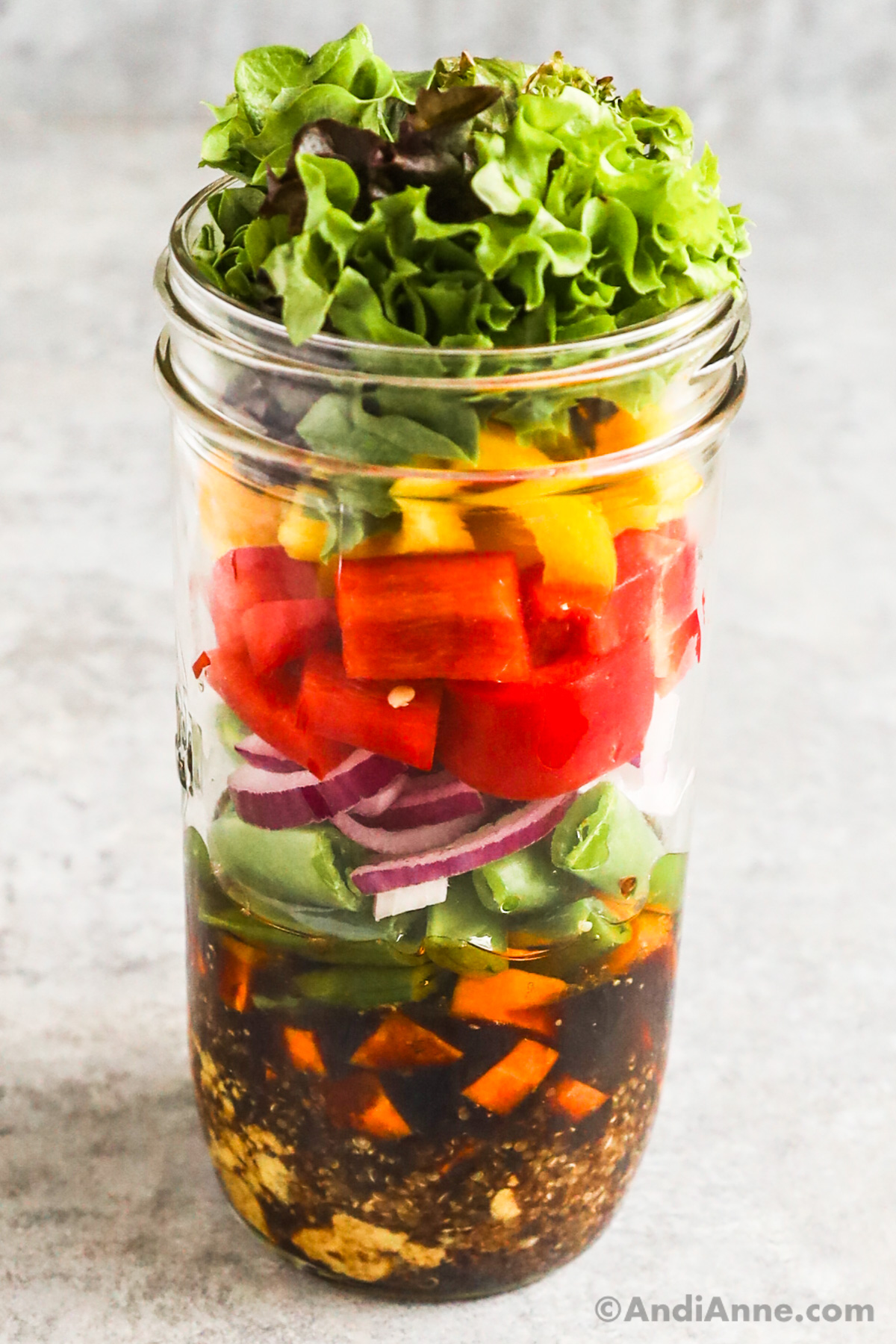 A rainbow mason jar salad with layers of dressing, quinoa, carrots, snap peas, onion, bell pepper and mixed greens.