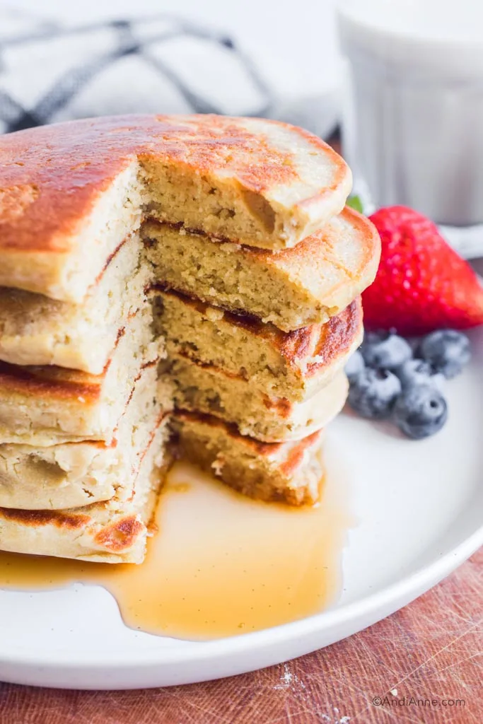 Stack of pancakes cut through. Berries in background. 