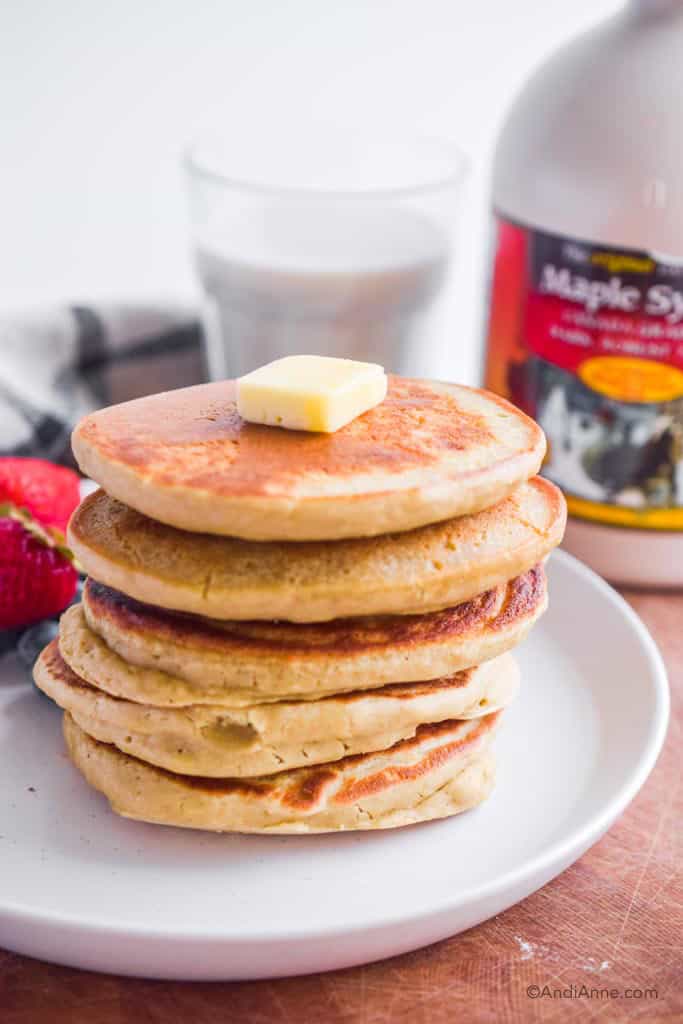 quinoa flour pancakes on white plate with butter on top. Glass of milk and maple syrup in background.