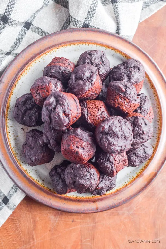 chocolate protein mini muffins on a large brown plate with kitchen towel beside it