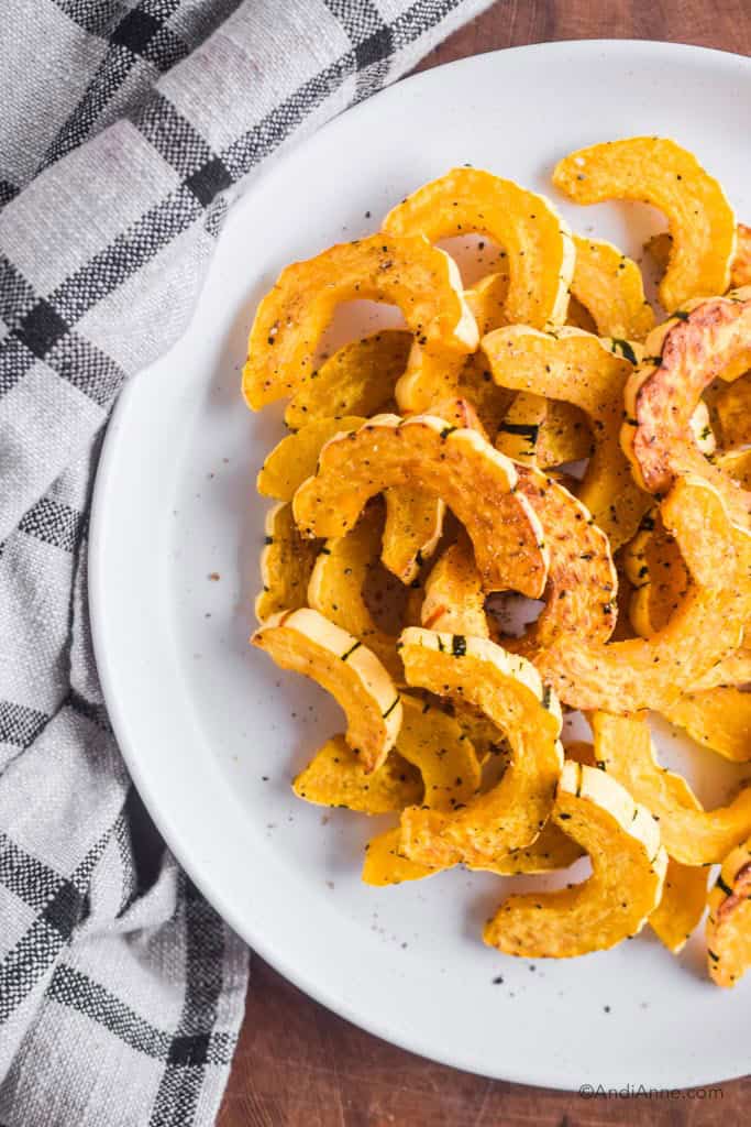 baked delicata squash on a white plate with kitchen towel beside it