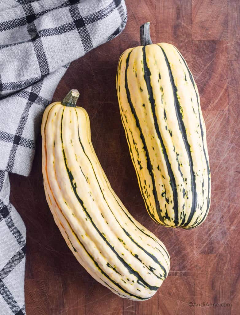 two delicata squash on a wood cutting board