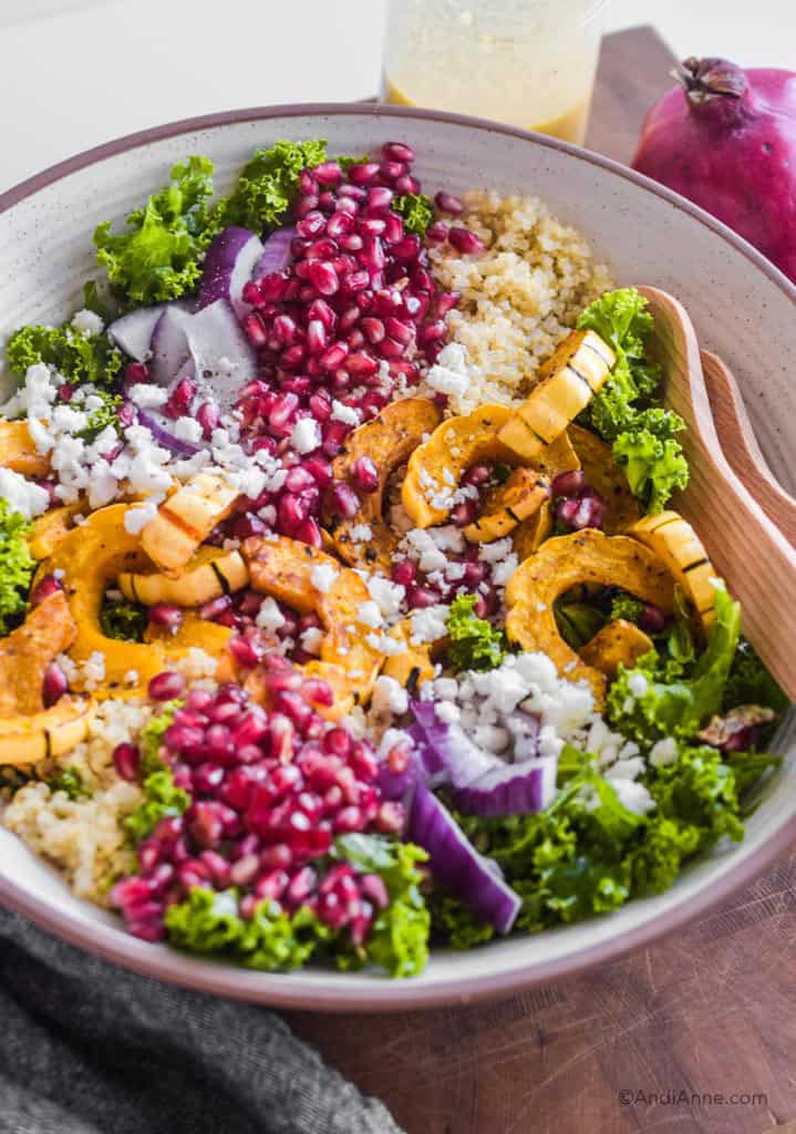 squash pomegranate kale quinoa salad in a white bowl with feta cheese