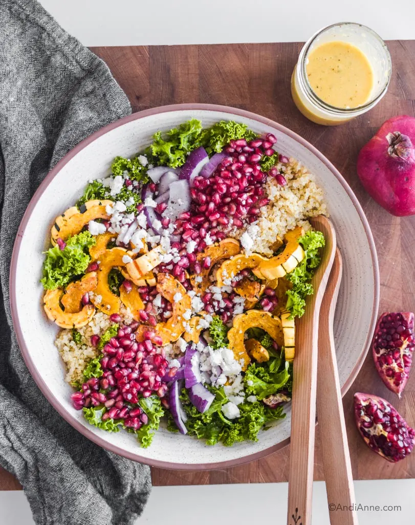 fall harvest salad in a white bowl with wooden spoons and pomegranate beside it