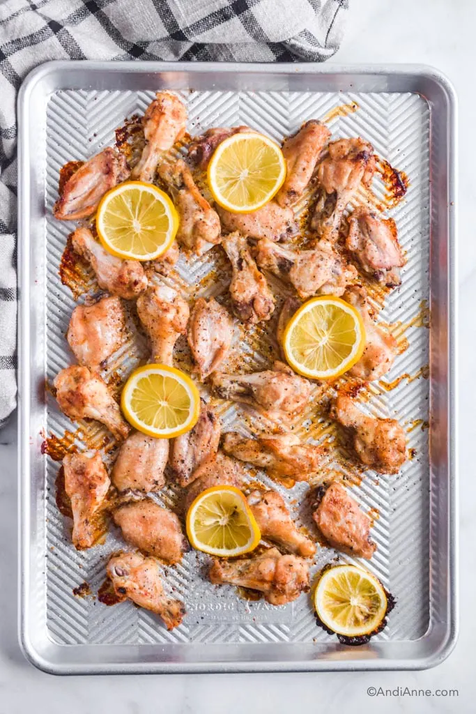 lemon garlic chicken wings on a silver baking sheet with sliced lemons