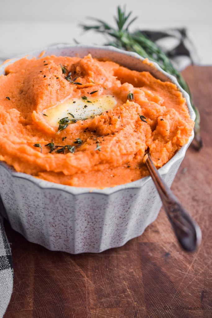 mashed sweet potatoes in a white bowl with melted butter and fresh thyme sprinkled on top. 