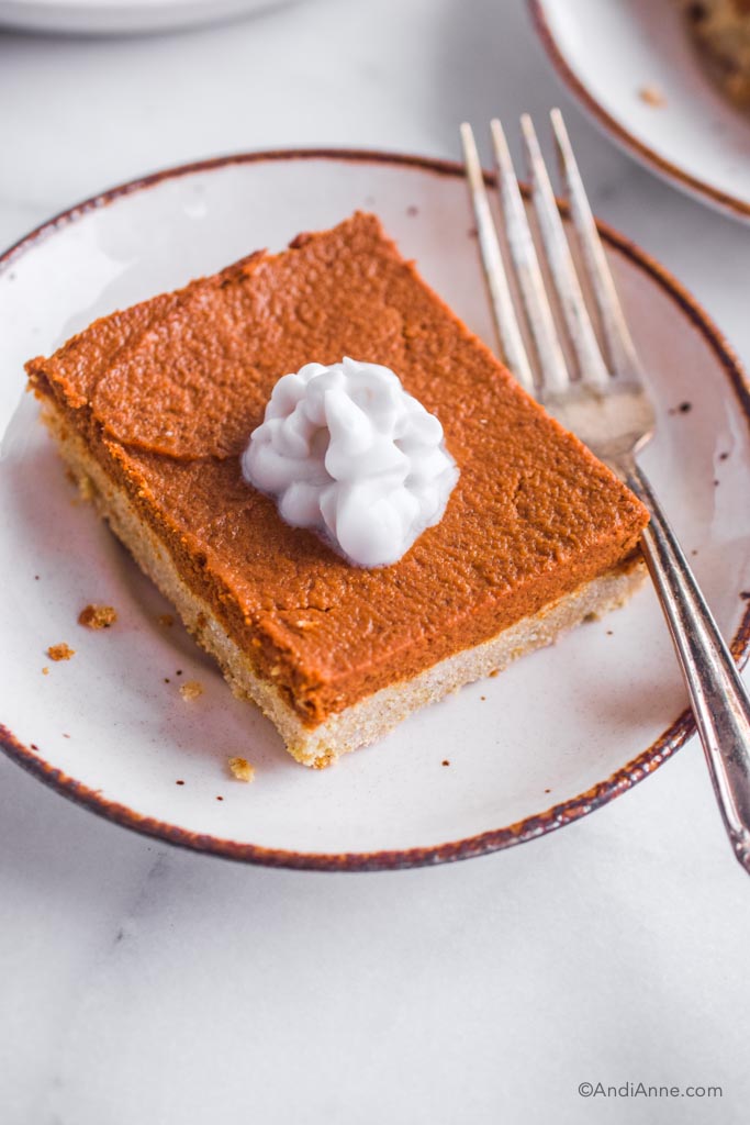 close up of slice of pumpkin pie bar with coconut cream on a white plate with a fork