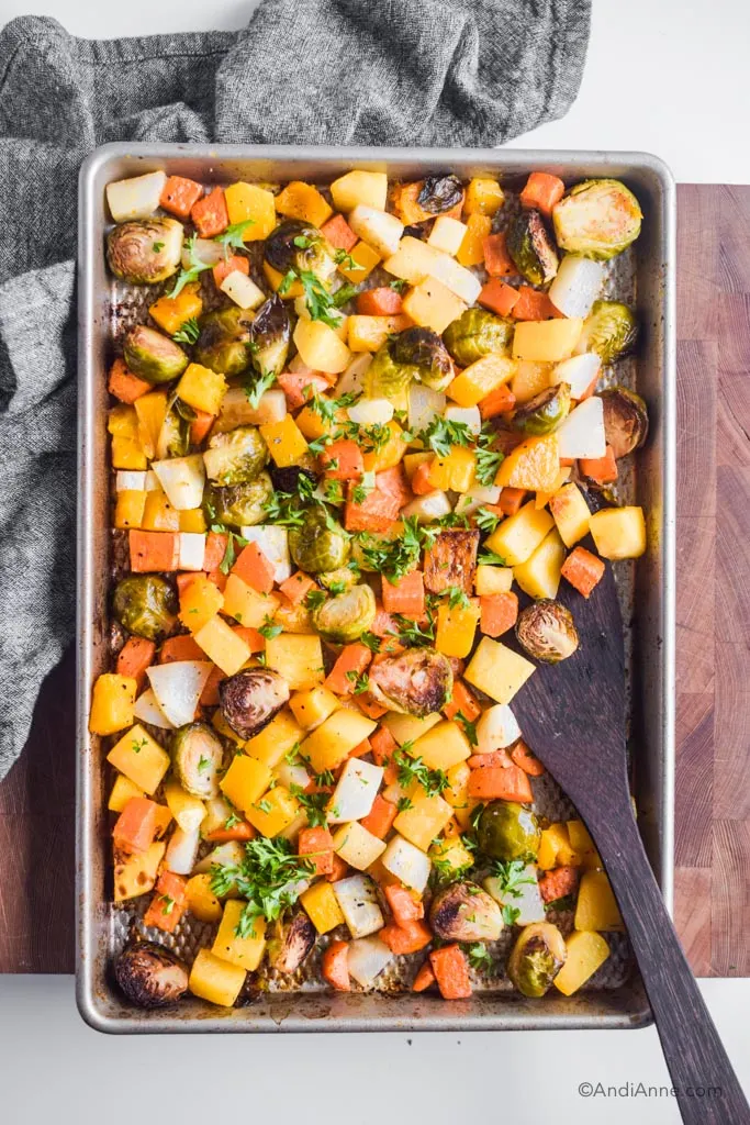Chopped roasted root vegetables on a baking sheet with wooden spatula on side. 