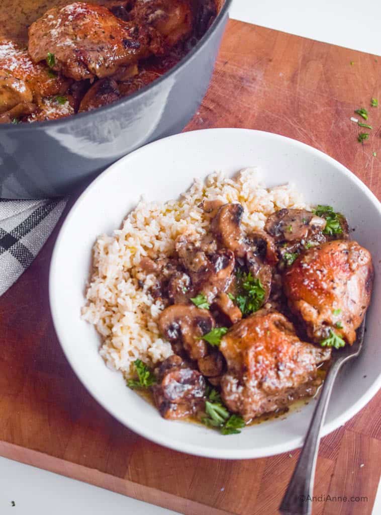 chicken thighs in mushroom sauce on a white plate with rice and a fork. Blue pot in background.