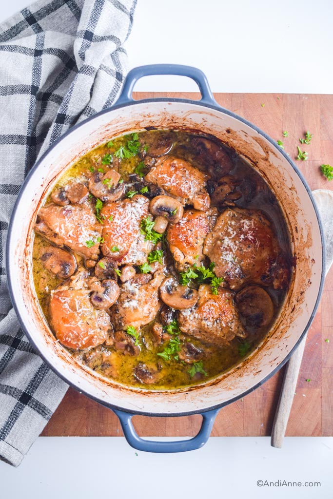 chicken thighs in a mushroom sauce in blue and white cast iron enamelled pot on a wood cutting board