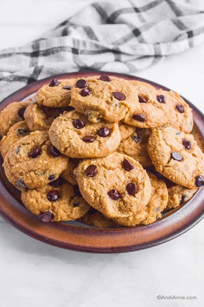 A plate of stacked chickpea chocolate chip cookies with kitchen towel in background.