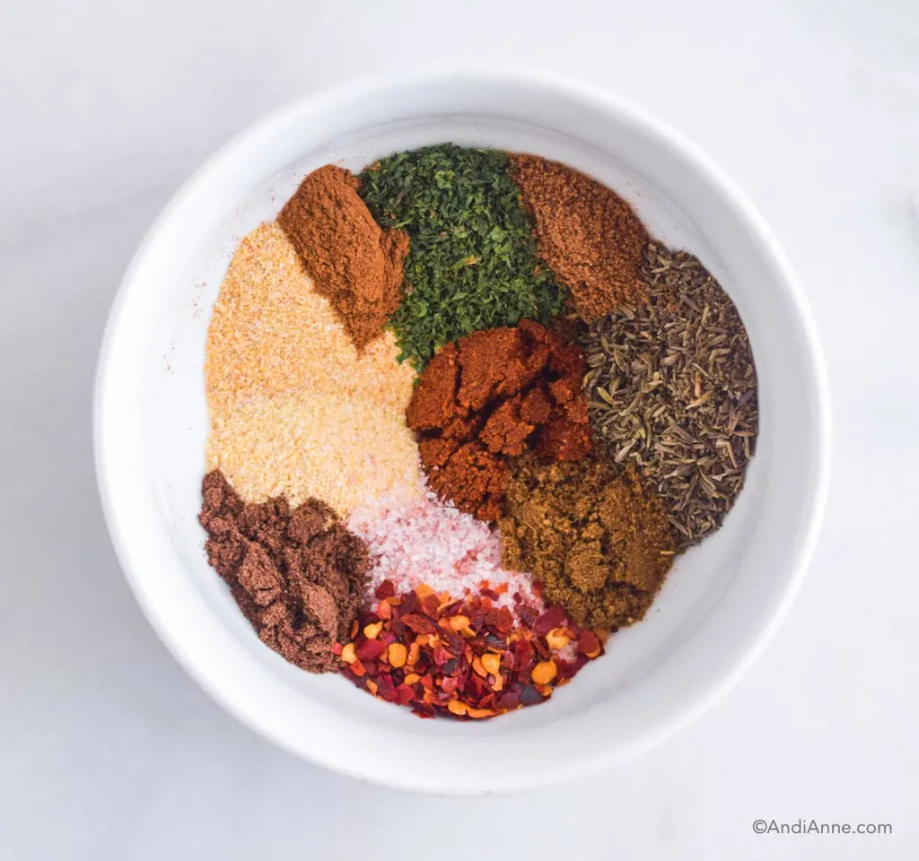 Looking down at a white bowl with a variety of spices poured in, unmixed.