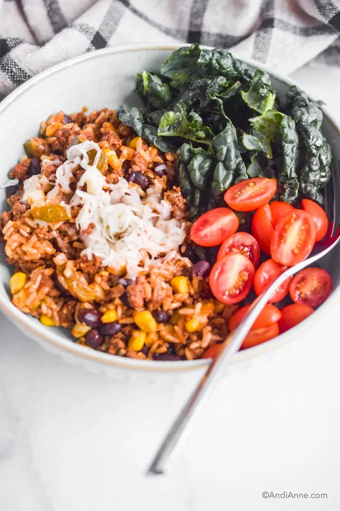 A bowl with rice, beef and beans, sliced cherry tomatoes, and kale and a fork. 
