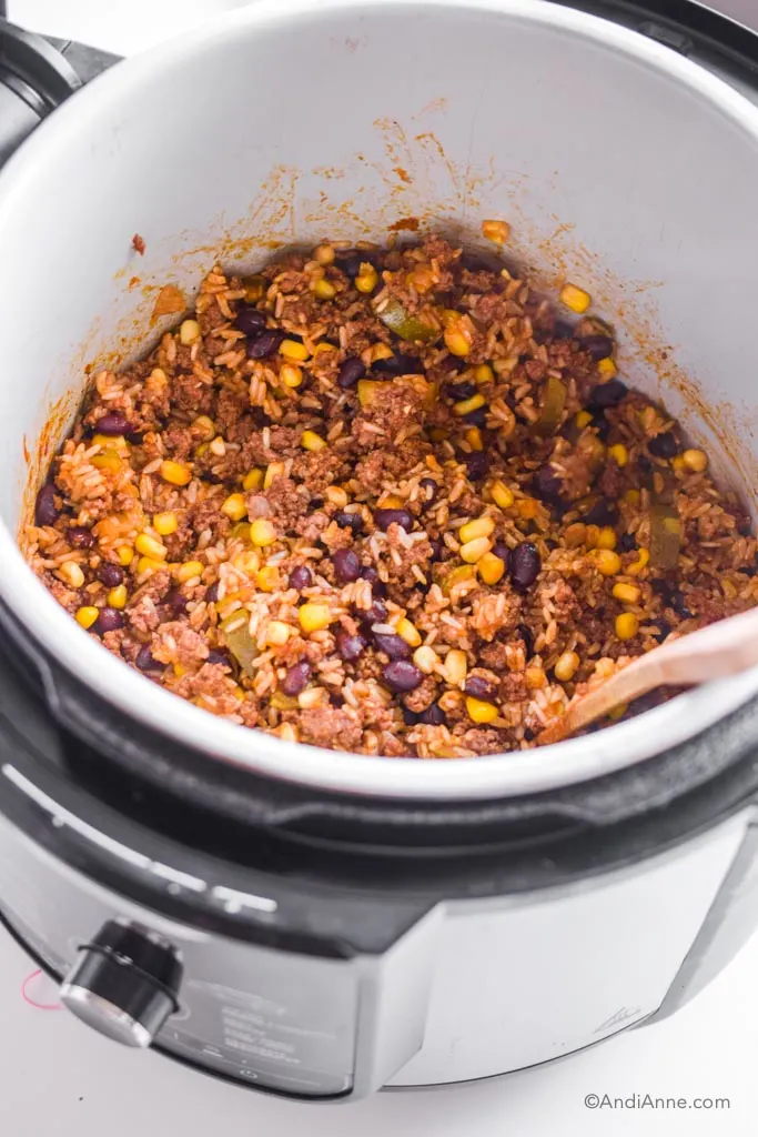 Looking into an instant pot with the burrito bowl rice mixture and a wood spatula.